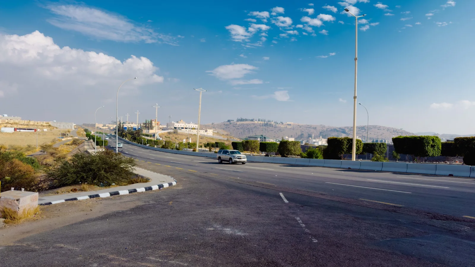Jalan raya di dataran tinggi Taif di bawah langit biru dengan bukit di kejauhan