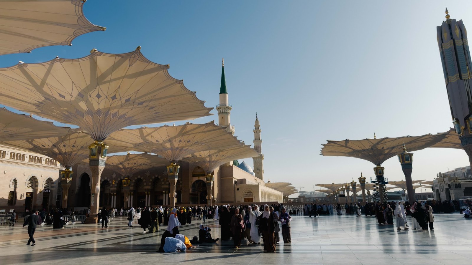 Payung gergasi dan menara Masjid Nabawi di Madinah dengan jemaah di dataran pada waktu pagi