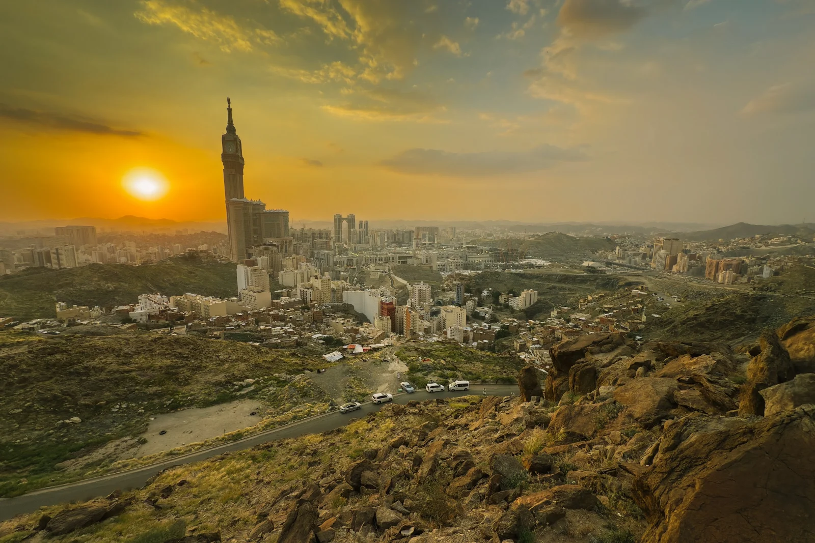 Kota Makkah dan menara jam Makkah ketika matahari terbenam, dilihat dari lereng bukit berbatu