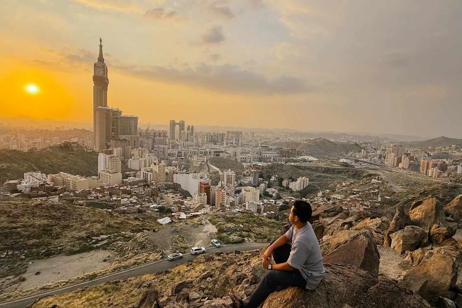 Kru AkuIslam duduk di atas batu bukit menghadap panorama senja kota Makkah