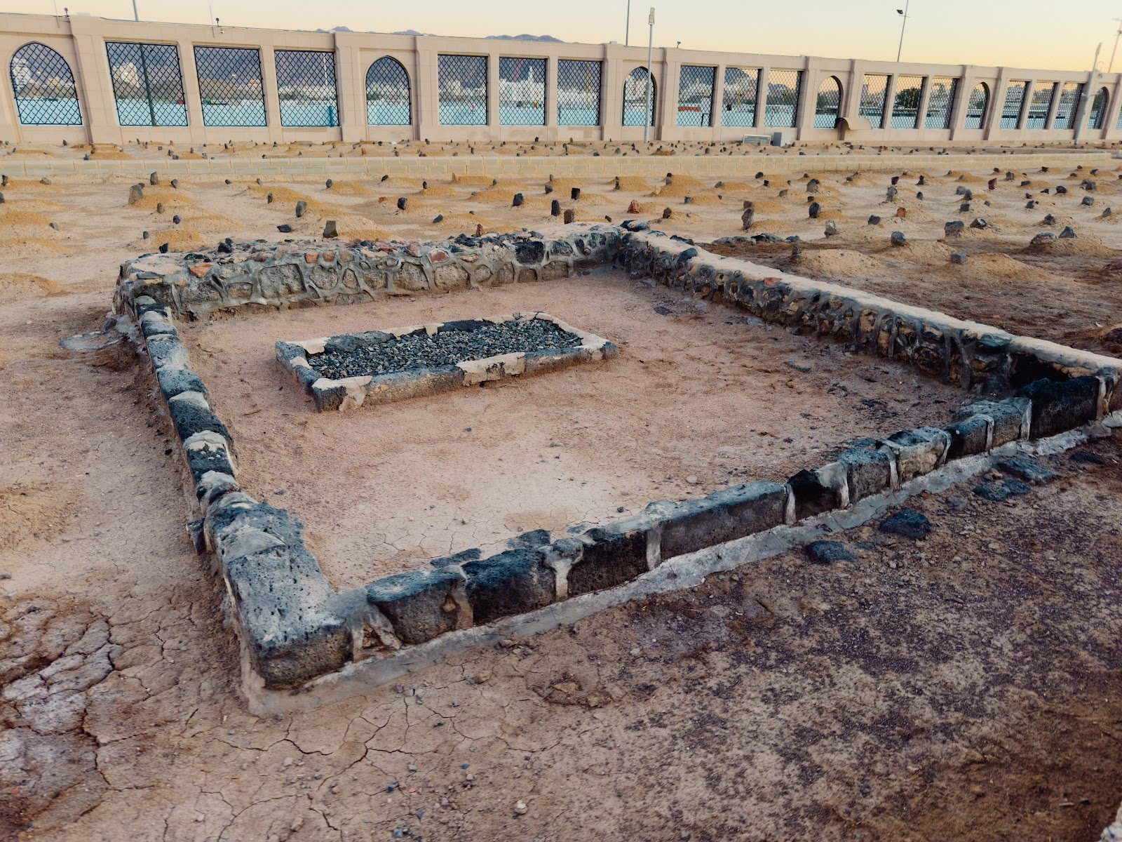 Kepungan batu sebuah makam di Perkuburan Baqi dengan tembok luar di belakangnya