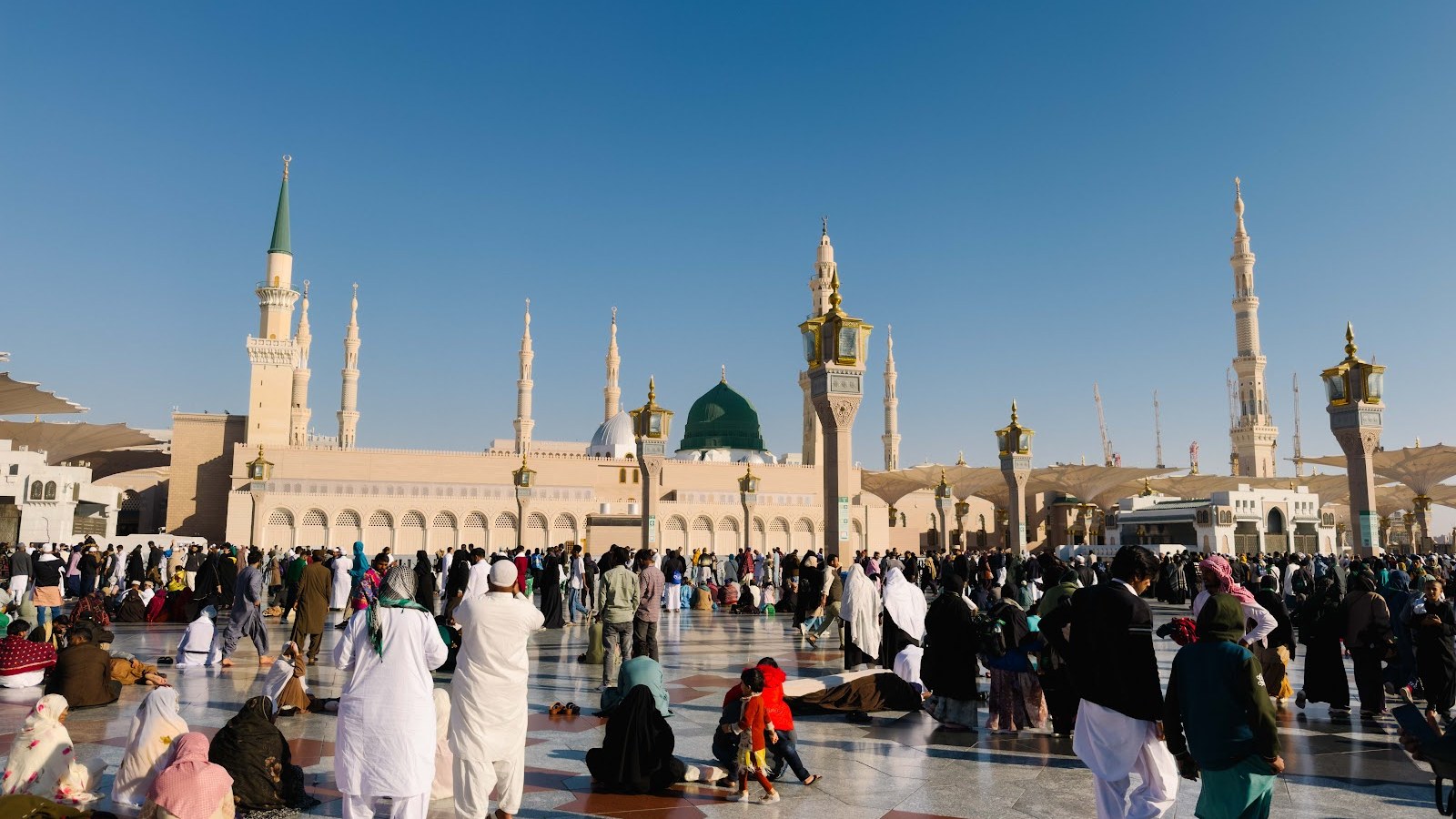 Jemaah di dataran Masjid Nabawi dengan Kubah Hijau dan menara di bawah langit biru