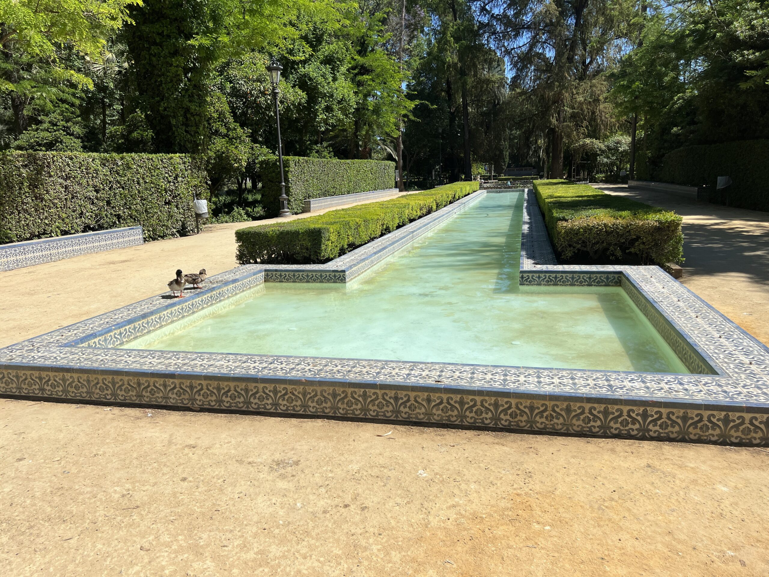 Kolam memanjang dengan pagar hijau di Taman María Luisa, Sevilla
