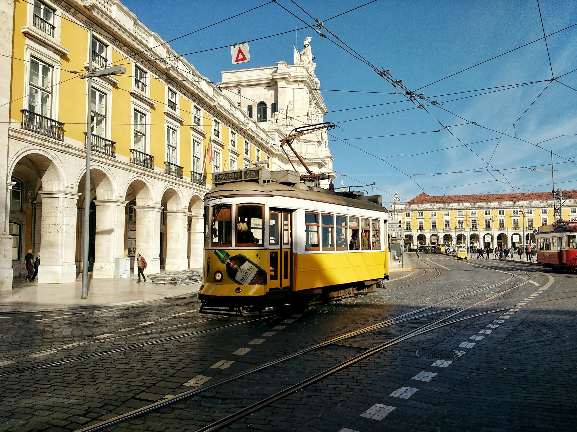 Tram kuning klasik melintasi kawasan Praça do Comércio