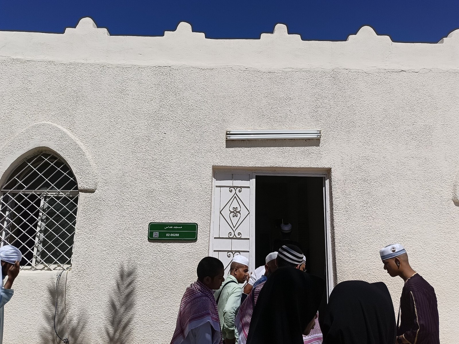 Pintu dan papan nama Masjid Addas dengan jemaah di hadapannya