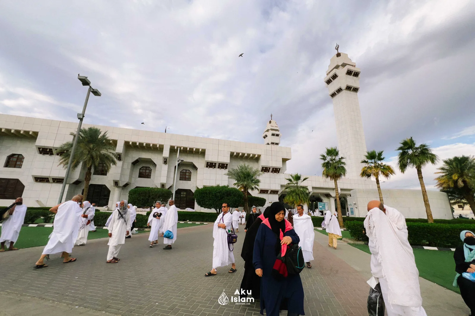 Jemaah berihram di halaman Masjid Aisyah dengan dua menara dan pohon kurma, Tan‘im