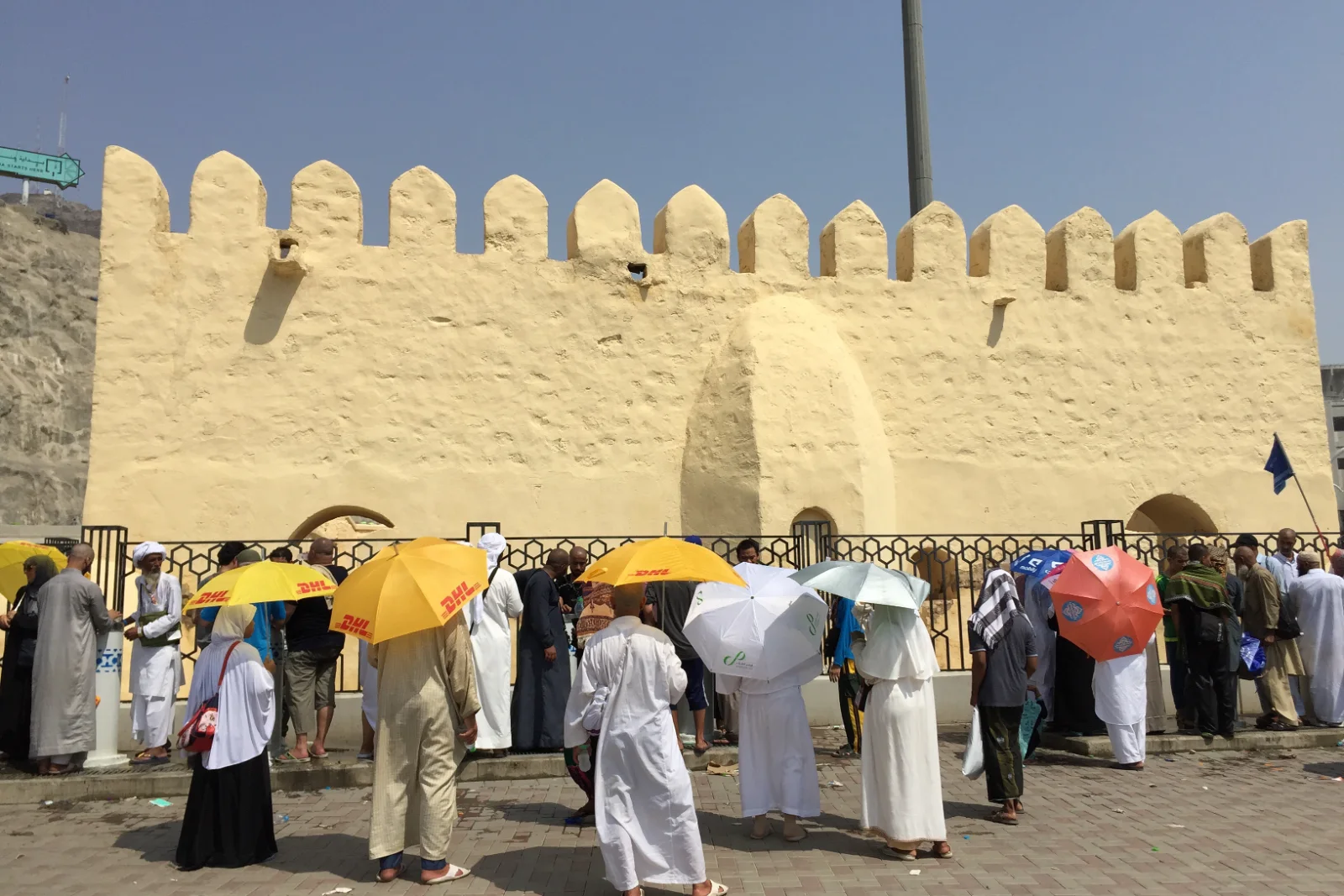 Jemaah haji berpayung berkumpul di luar dinding Masjid al-Bai‘ah, Mina