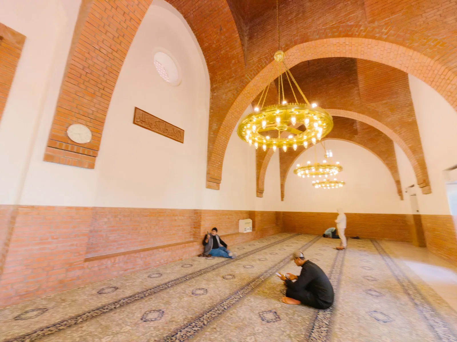 Ruang solat Masjid Ali bin Abi Talib dengan lengkungan bata dan candelier