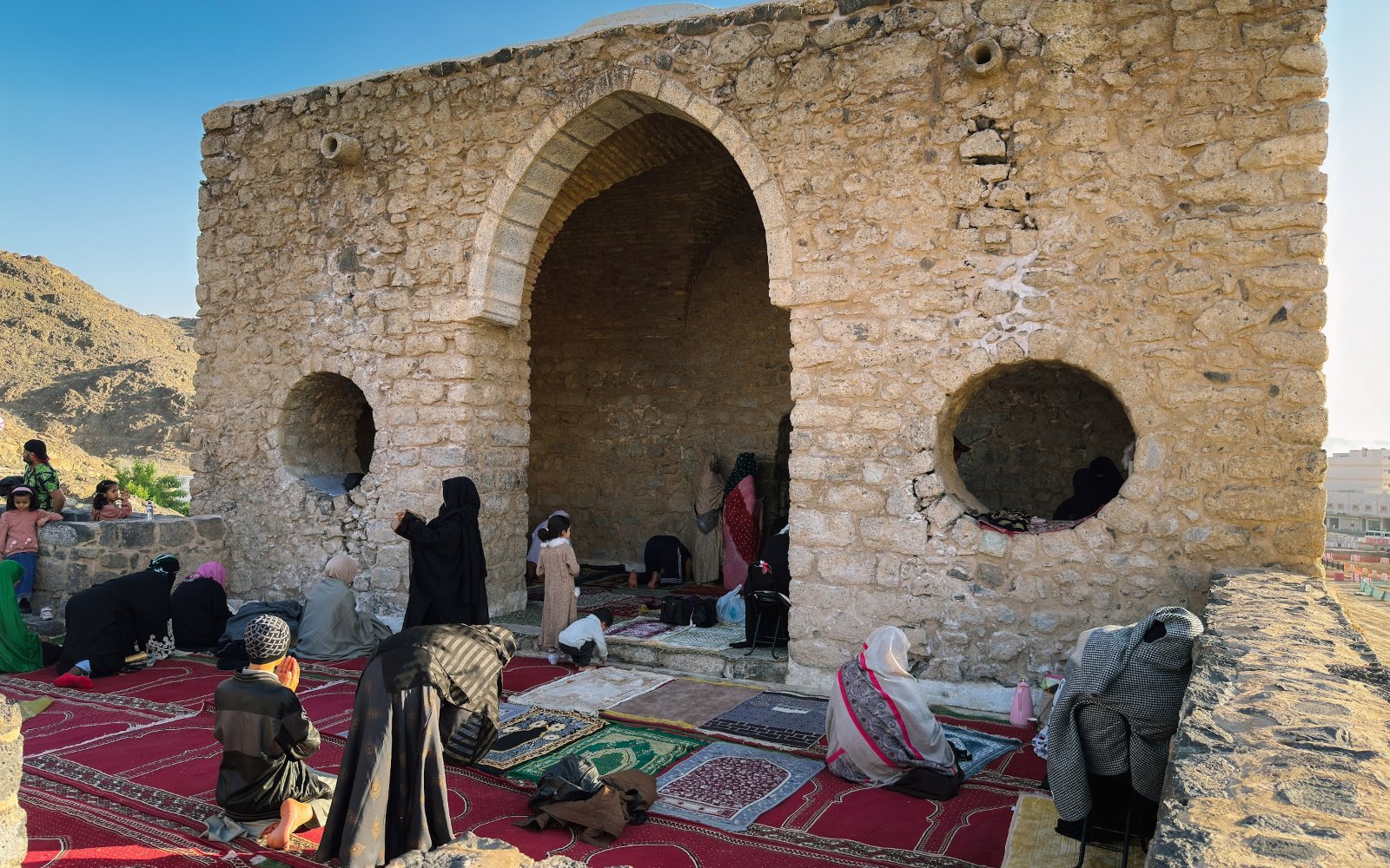 Jemaah duduk di hadapan masjid batu kecil bergerbang di kawasan Masjid Tujuh, Madinah