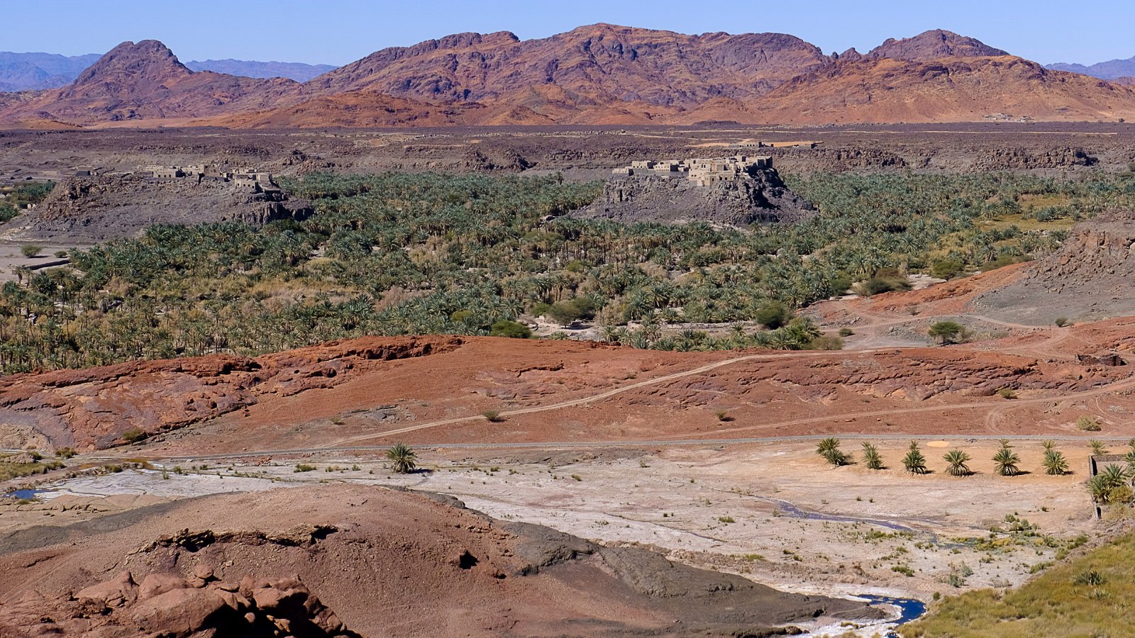 Lembah oasis Khaibar dengan kebun kurma, tanah batu gelap dan banjaran bukit di kejauhan