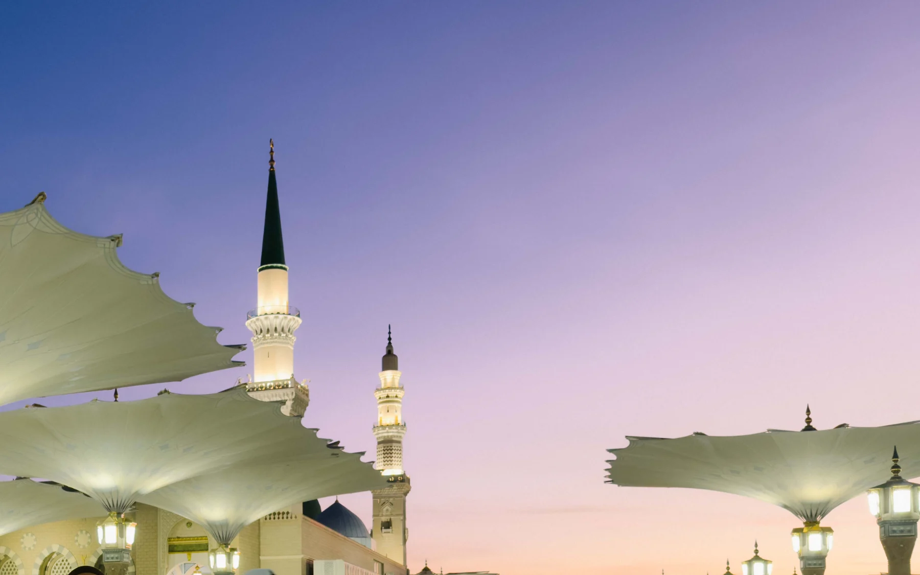Menara Masjid Nabawi dan payung gergasi di dataran masjid ketika senja, Madinah
