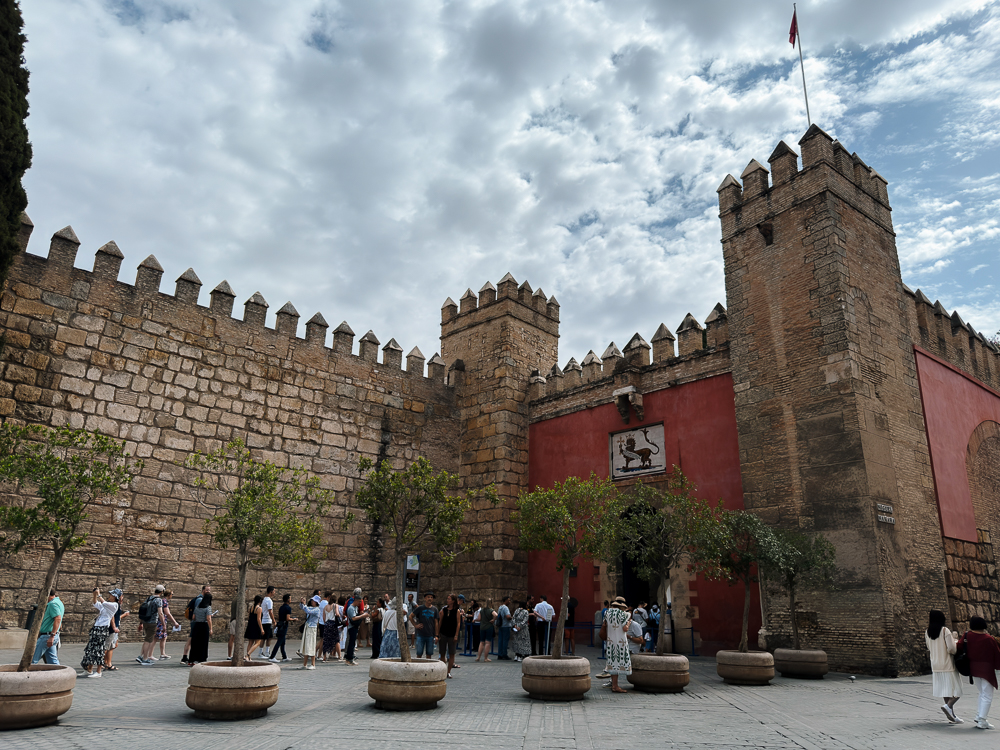 Tembok Real Alcázar Sevilla dan Puerta del León dengan barisan pengunjung