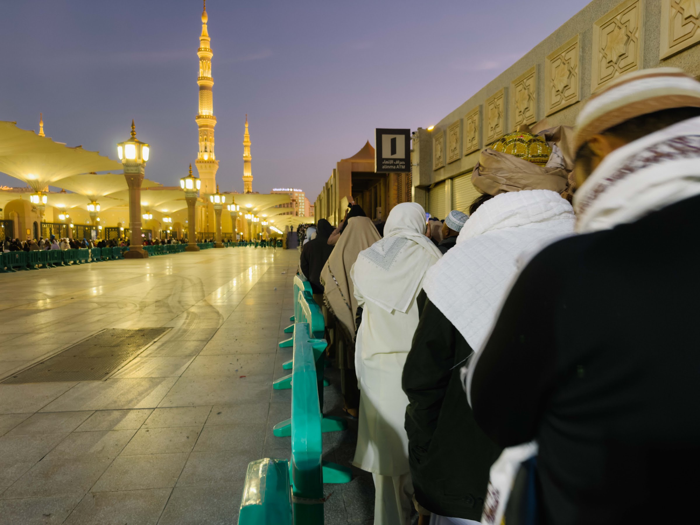Jemaah beratur menuju Masjid Nabawi pada awal pagi dengan menara bercahaya di hujung dataran