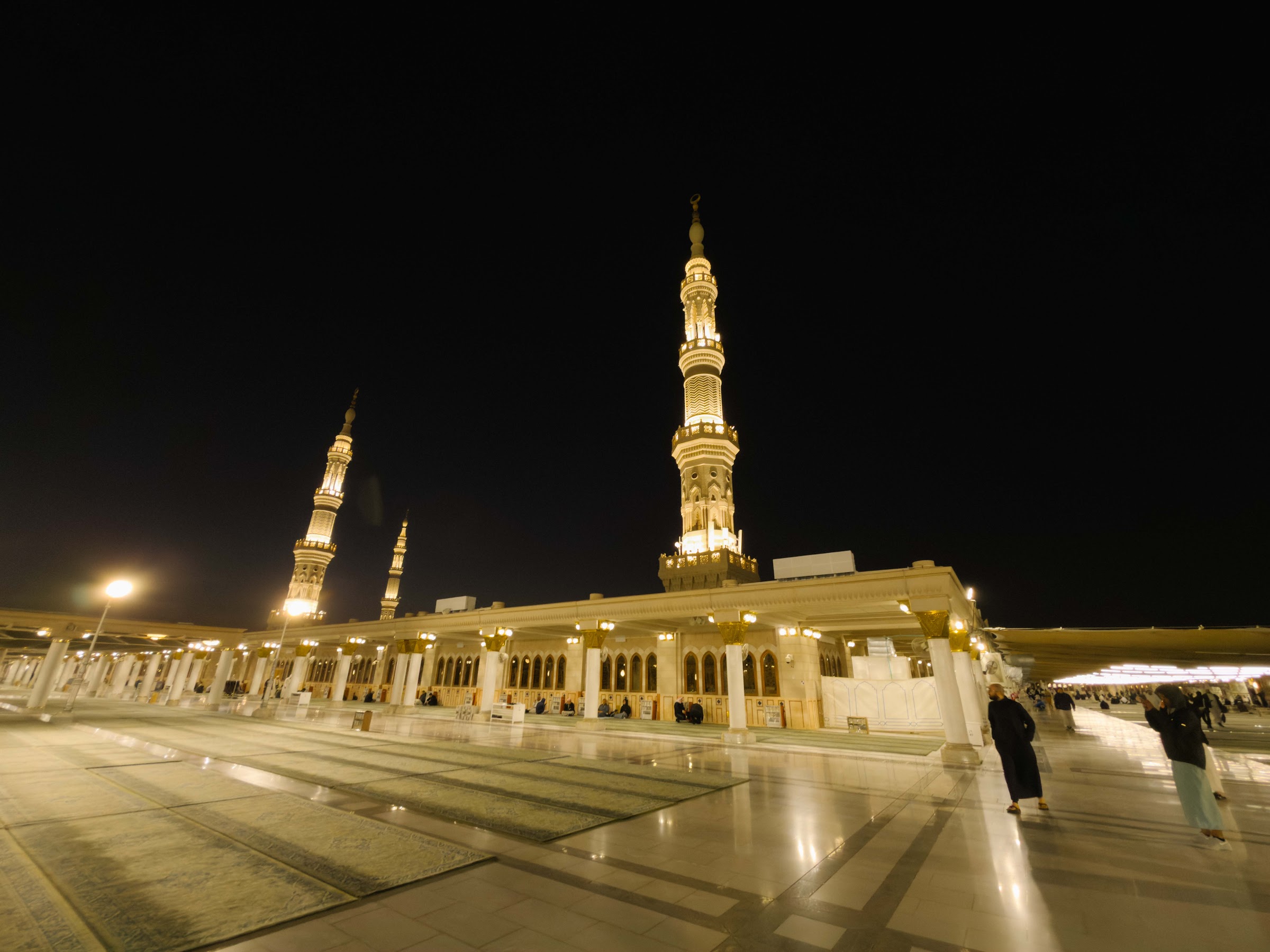 Menara Masjid Nabawi bercahaya pada waktu malam dengan dataran masjid yang lapang