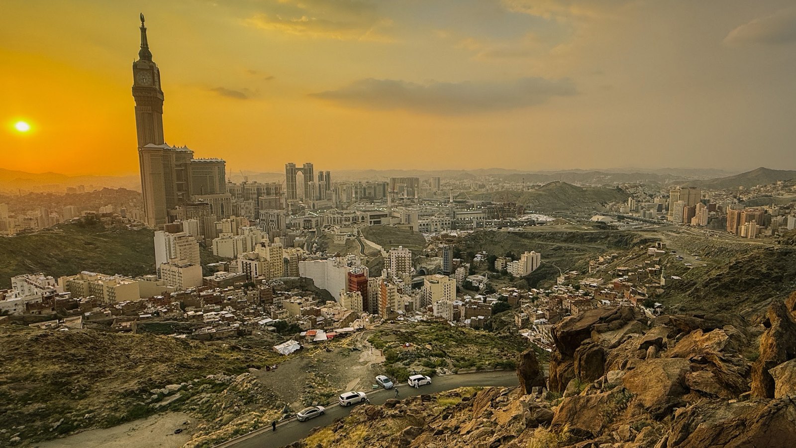 Pemandangan kota Makkah ketika senja dari sebuah bukit, dengan menara jam dan matahari terbenam