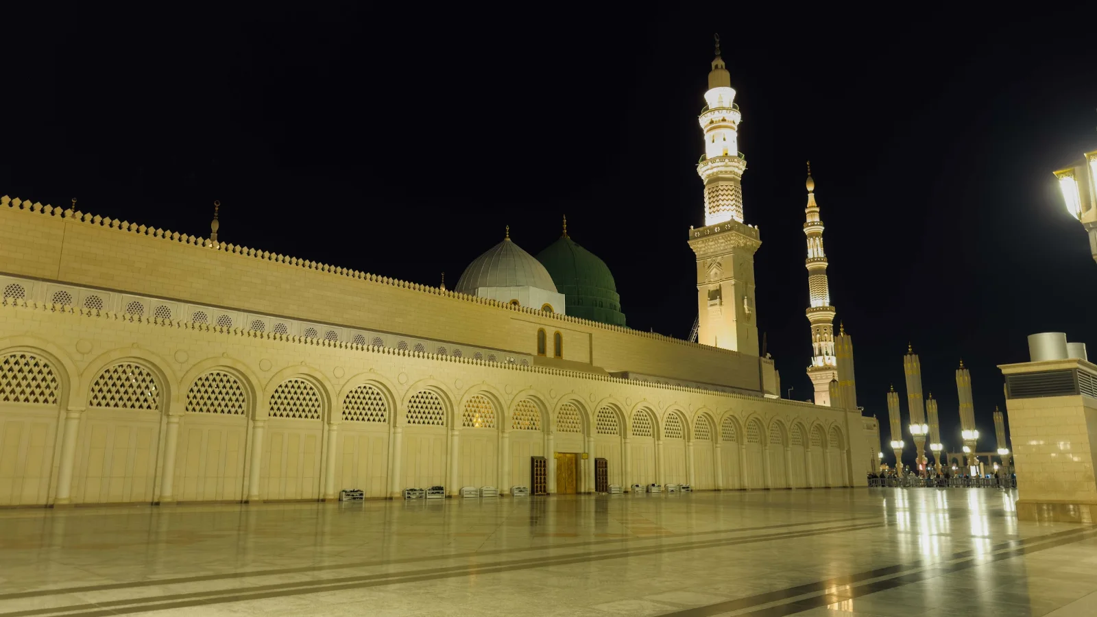 Halaman Masjid Nabawi pada waktu malam dengan menara dan kubah hijau