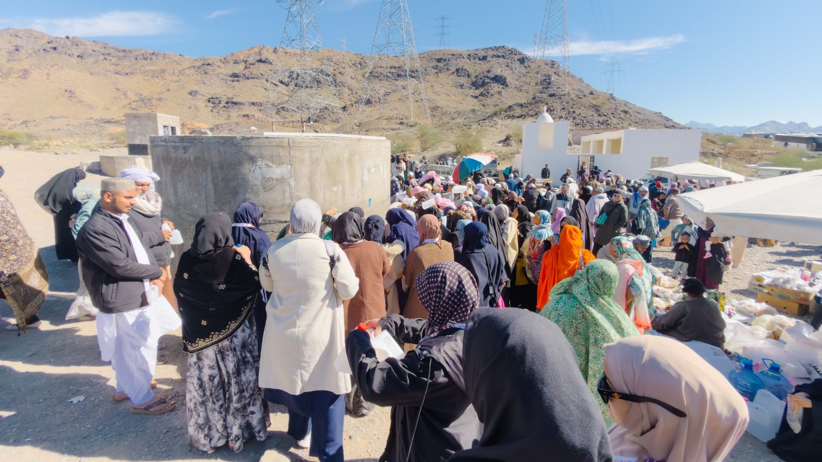 Tangki air bulat Telaga Syifa dengan jemaah, bukit berbatu dan menara elektrik di laluan Madinah ke Badar